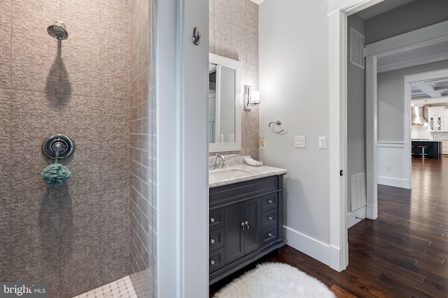 bathroom with visible vents, vanity, wood finished floors, baseboards, and tiled shower