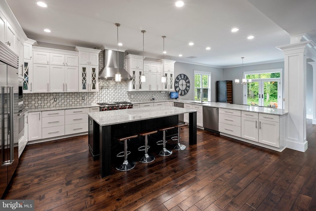 kitchen with wall chimney range hood, appliances with stainless steel finishes, decorative backsplash, and a peninsula