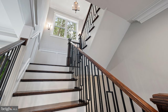 stairway with ornamental molding, a decorative wall, and a notable chandelier