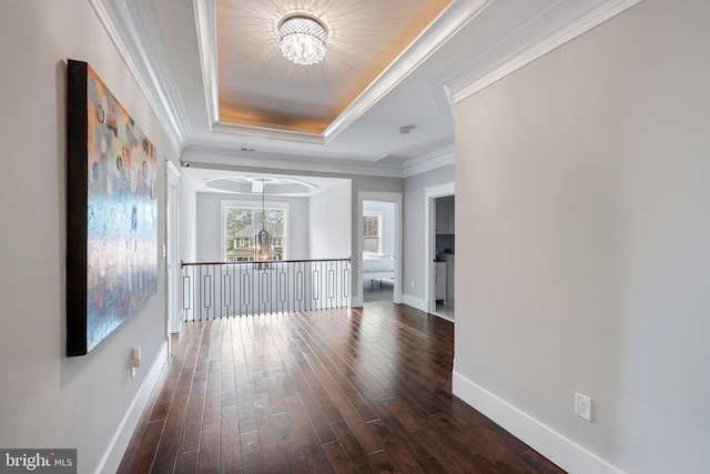 hall with an inviting chandelier, a raised ceiling, dark wood-type flooring, and baseboards