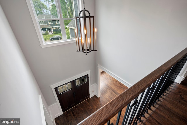 entryway with a towering ceiling, a notable chandelier, dark wood-type flooring, and baseboards