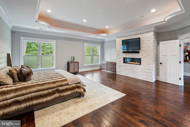 bedroom with crown molding, a stone fireplace, and a raised ceiling