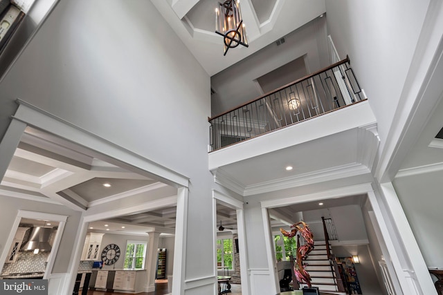 interior space featuring stairs, ornamental molding, a high ceiling, coffered ceiling, and ornate columns