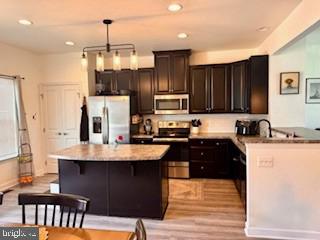 kitchen with dark brown cabinets, light wood-style flooring, a center island, stainless steel appliances, and pendant lighting