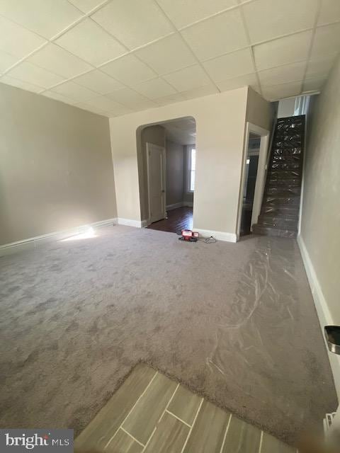 interior space featuring carpet floors, arched walkways, baseboards, and a paneled ceiling