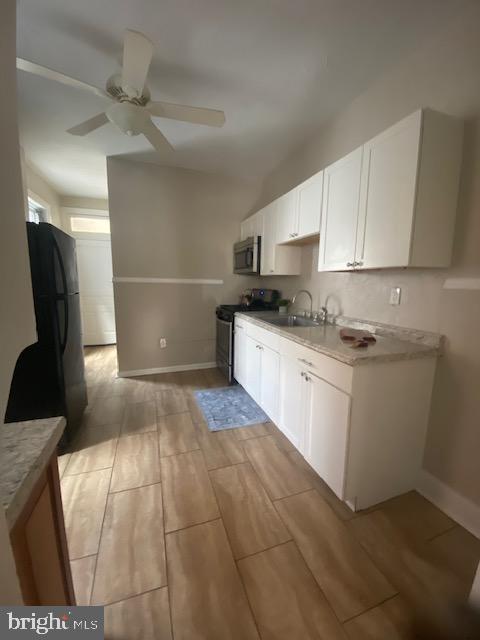 kitchen with a ceiling fan, appliances with stainless steel finishes, wood finish floors, a sink, and baseboards