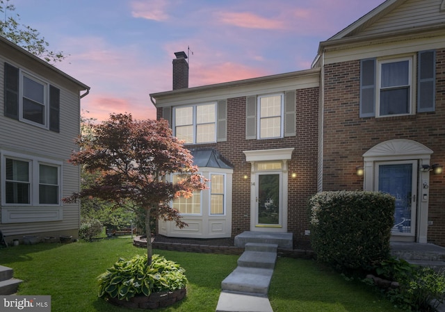 townhome / multi-family property with a lawn, brick siding, and a chimney