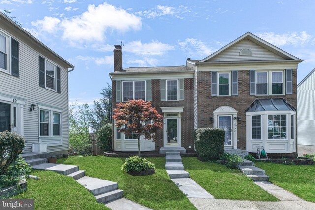 townhome / multi-family property with entry steps, a chimney, brick siding, and a front yard