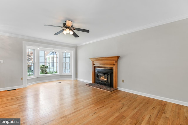 unfurnished living room with ornamental molding, a lit fireplace, light wood-type flooring, and ceiling fan