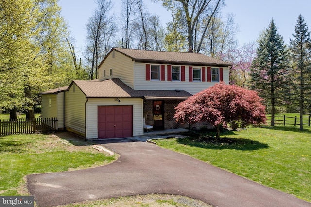 traditional-style house with fence, an attached garage, a shingled roof, a front lawn, and aphalt driveway