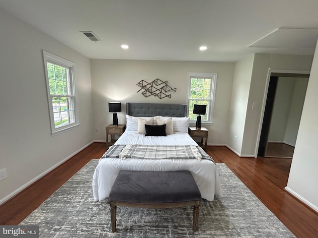 bedroom with attic access, baseboards, visible vents, and wood finished floors