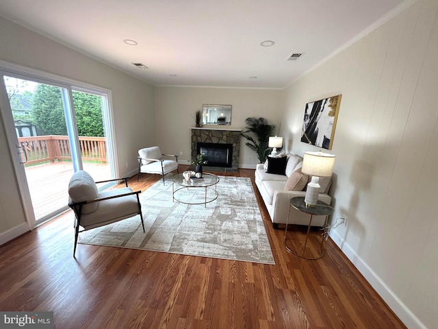 living room with wood finished floors, a fireplace, visible vents, baseboards, and ornamental molding