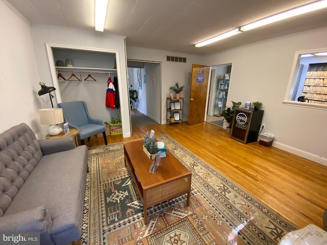 living area with crown molding, baseboards, wood finished floors, and visible vents