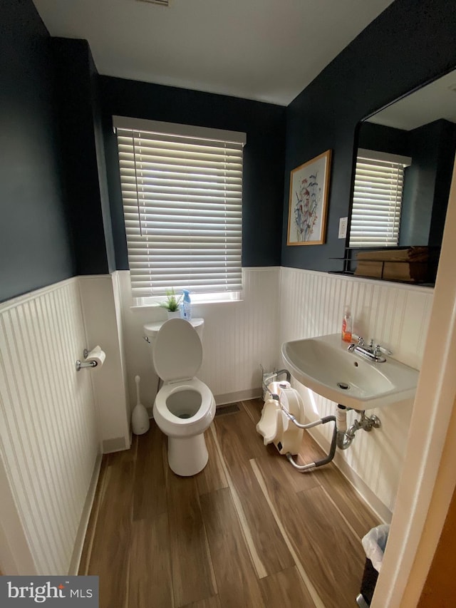bathroom with wainscoting, wood finished floors, toilet, plenty of natural light, and a sink