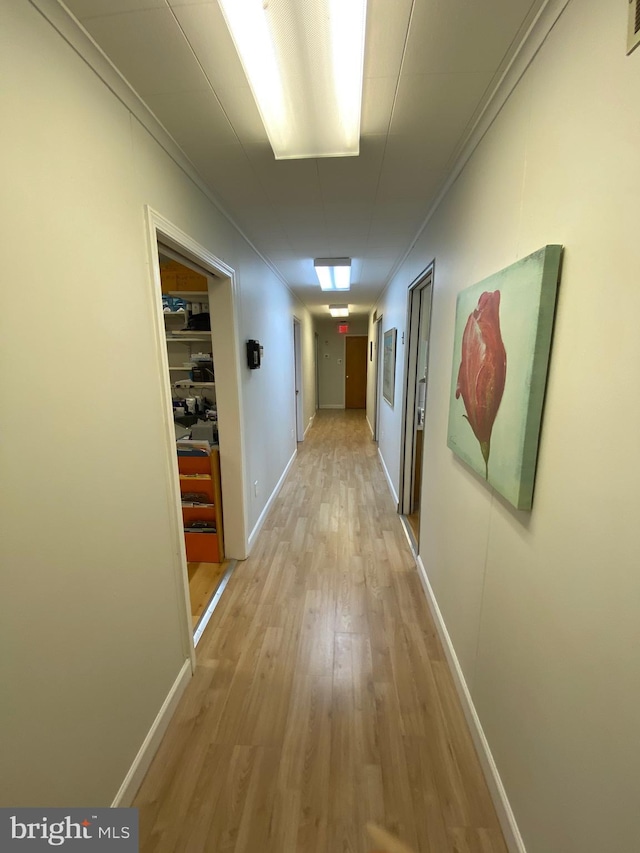 corridor featuring light wood-style floors, baseboards, ornamental molding, and visible vents