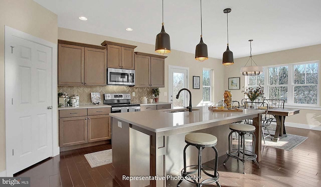 kitchen featuring a sink, a kitchen island with sink, light countertops, stainless steel appliances, and dark wood-style floors