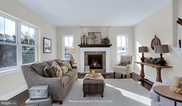 living area with a stone fireplace, stairs, baseboards, and wood finished floors