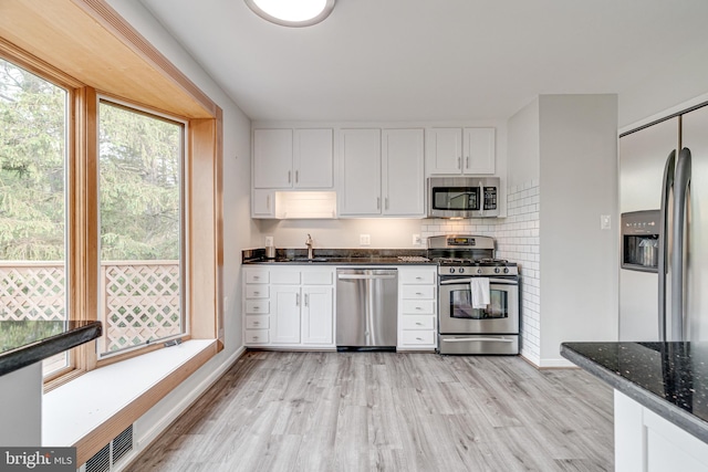 kitchen featuring white cabinets, dark stone counters, stainless steel appliances, baseboards, and light wood-type flooring