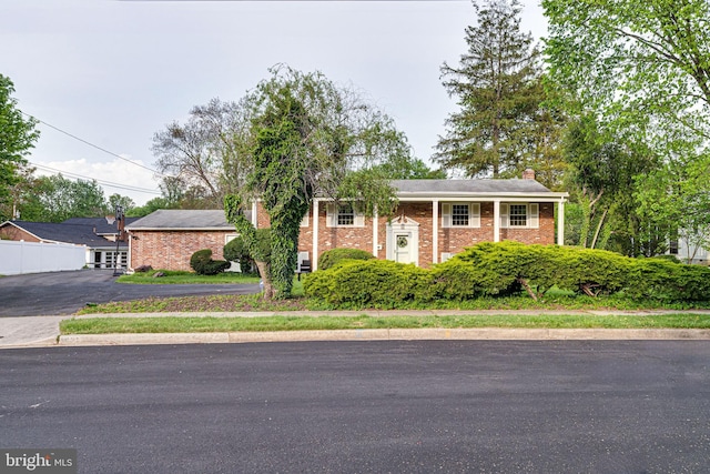 bi-level home with brick siding, fence, driveway, and a chimney