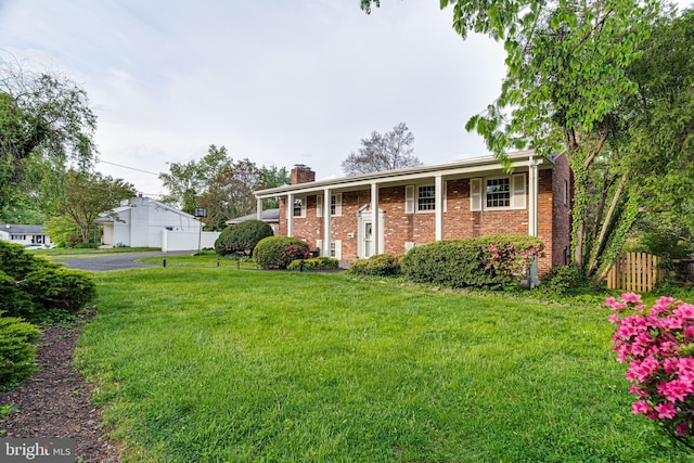 split foyer home featuring brick siding, a front lawn, fence, and a chimney