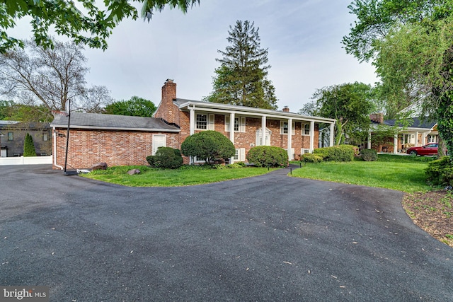 view of front of house with brick siding, a chimney, and a front yard