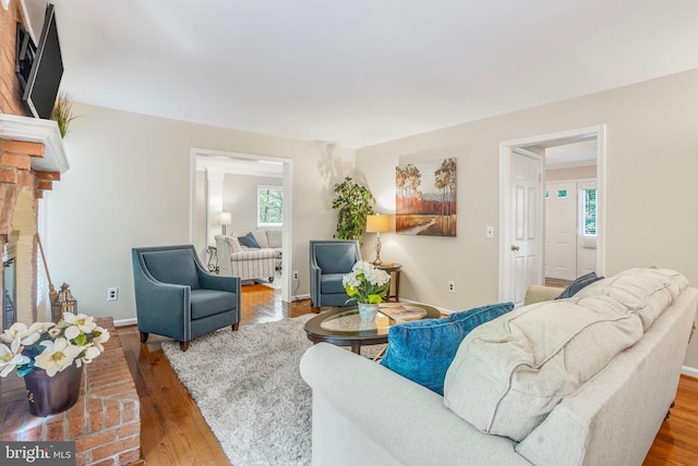 living area featuring baseboards, a brick fireplace, and wood finished floors