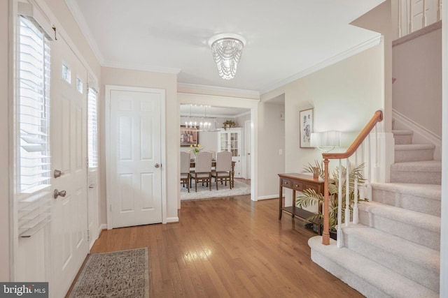 entrance foyer with crown molding, an inviting chandelier, wood finished floors, and stairway