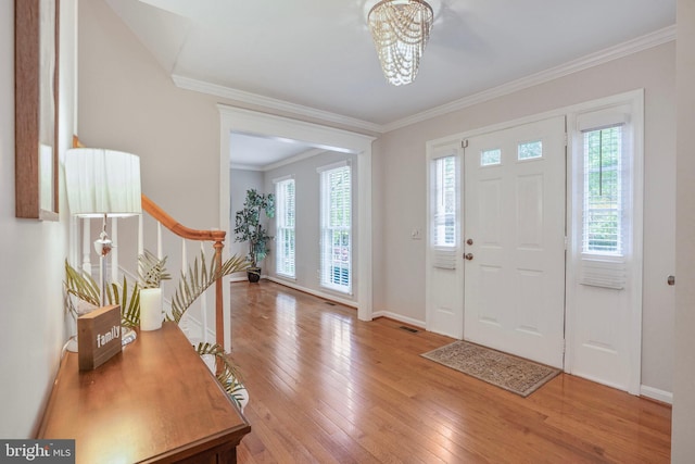 foyer featuring a healthy amount of sunlight, ornamental molding, wood-type flooring, and a notable chandelier