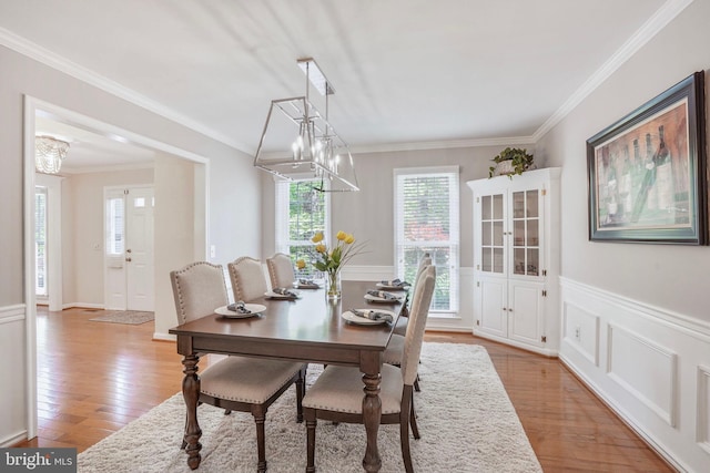 dining space with light wood-type flooring, ornamental molding, wainscoting, and an inviting chandelier