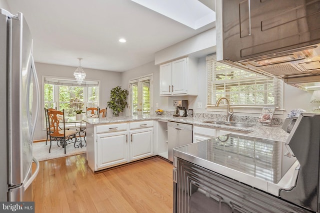 kitchen featuring a sink, a peninsula, light wood-style floors, stainless steel appliances, and white cabinetry