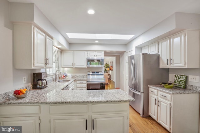 kitchen featuring a skylight, appliances with stainless steel finishes, a peninsula, and a sink