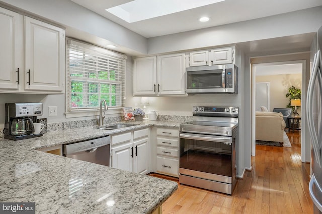 kitchen featuring a sink, a skylight, stainless steel appliances, and white cabinetry