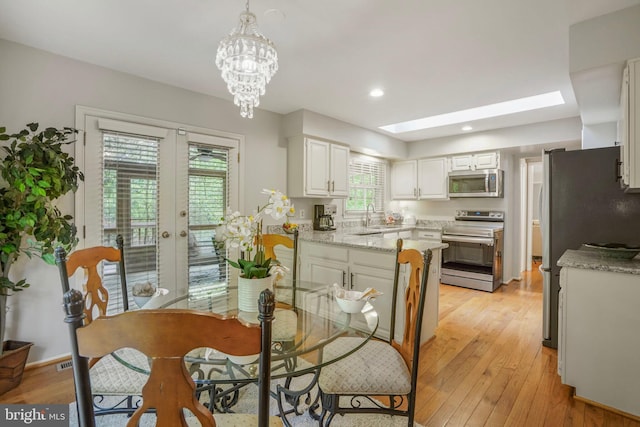 dining room with an inviting chandelier, light wood-type flooring, recessed lighting, french doors, and a skylight