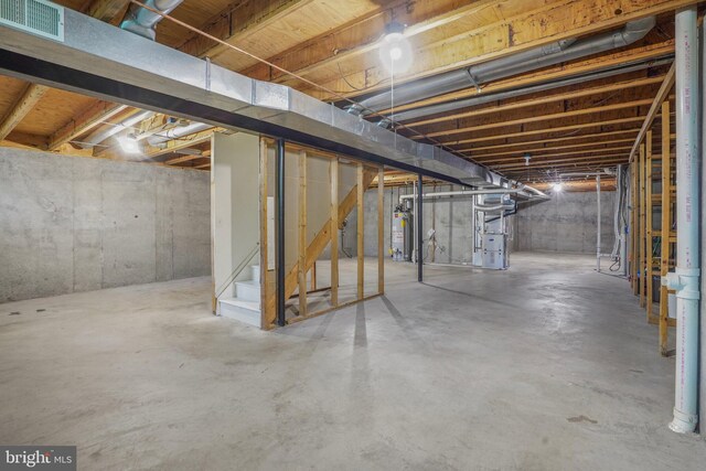 unfinished basement featuring visible vents, heating unit, water heater, and stairs