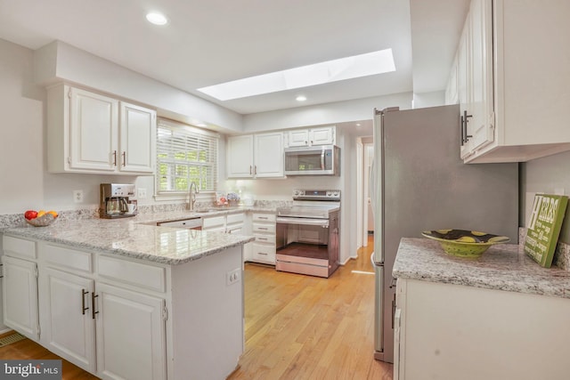 kitchen featuring a skylight, appliances with stainless steel finishes, light wood-type flooring, and a peninsula
