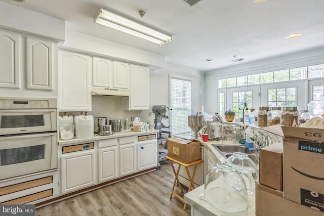 kitchen with white double oven, white cabinets, under cabinet range hood, and light wood-type flooring