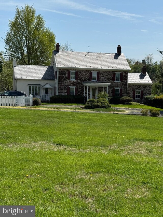 view of front facade featuring a chimney, stone siding, and a front yard