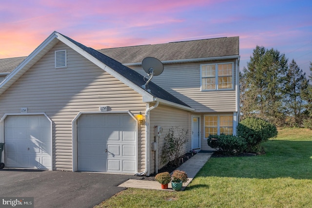 traditional-style house featuring an attached garage, a shingled roof, a front lawn, and aphalt driveway
