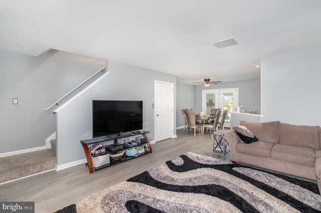 living room with ceiling fan, visible vents, wood finished floors, baseboards, and stairs