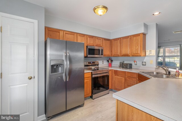 kitchen featuring appliances with stainless steel finishes, a sink, light countertops, brown cabinetry, and light wood-type flooring