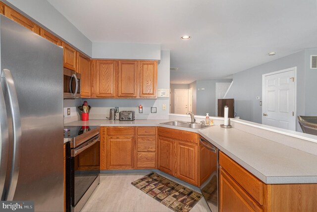 kitchen featuring a peninsula, light wood-type flooring, light countertops, a sink, and stainless steel appliances