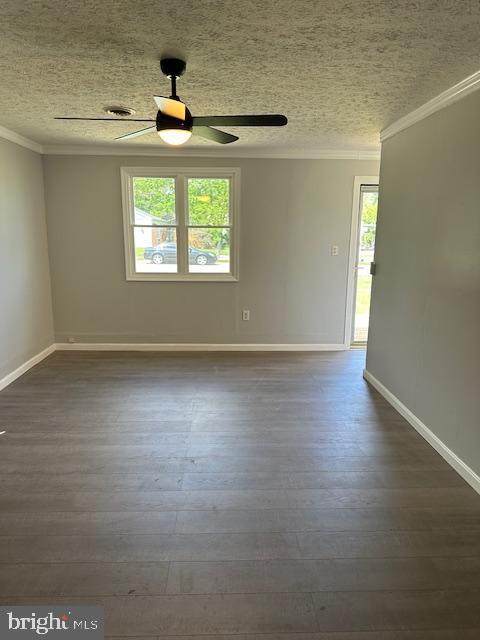 spare room with crown molding, a ceiling fan, dark wood-style flooring, and a healthy amount of sunlight