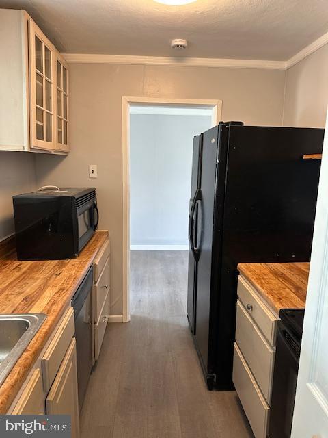 kitchen featuring a sink, wood finished floors, ornamental molding, glass insert cabinets, and black appliances