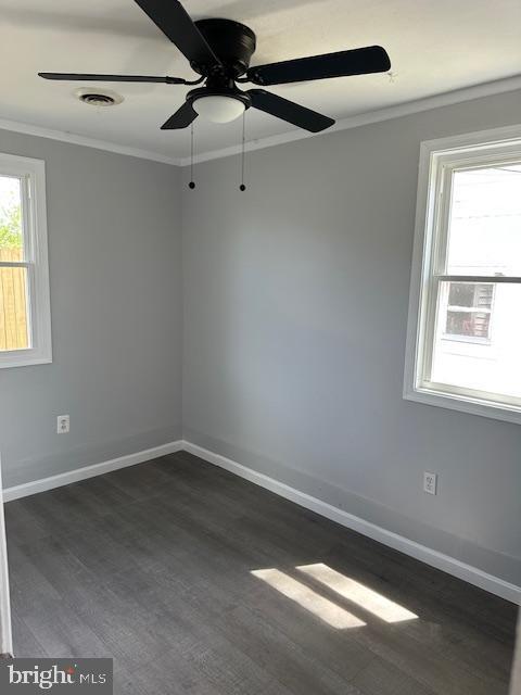 empty room with visible vents, ornamental molding, baseboards, ceiling fan, and dark wood-style floors