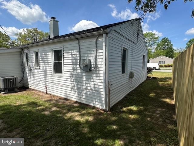 view of home's exterior featuring fence, central AC unit, a chimney, and a yard