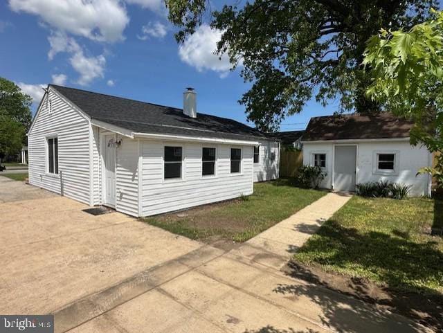 back of property featuring a lawn, concrete driveway, and a chimney