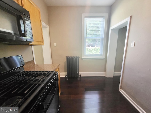 kitchen featuring light brown cabinetry, dark wood-style flooring, radiator, baseboards, and black appliances