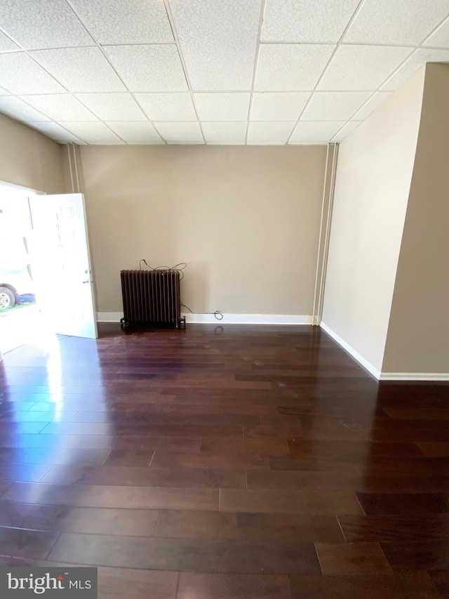 unfurnished room with a paneled ceiling, baseboards, wood finished floors, and radiator