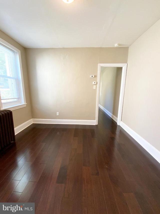 empty room with baseboards, dark wood-style flooring, and radiator