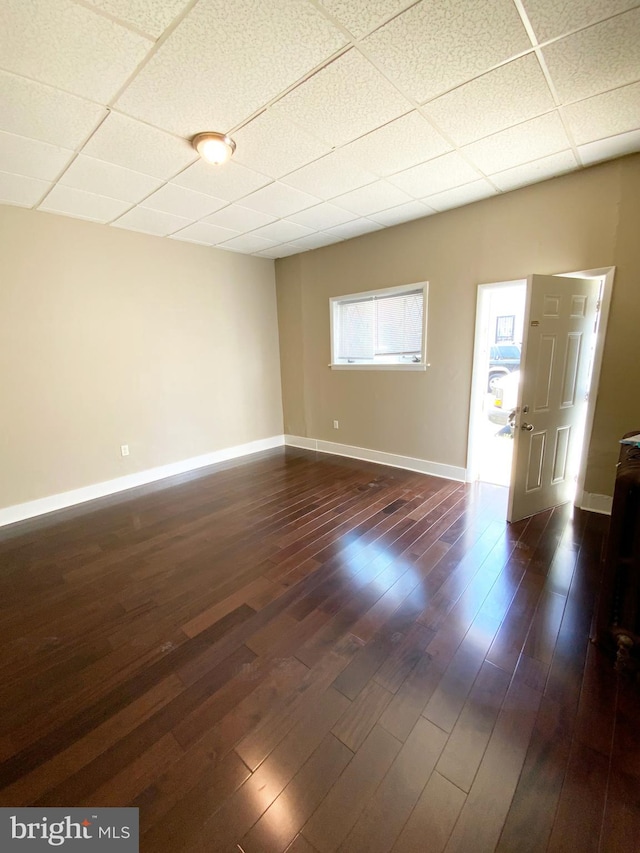 unfurnished room featuring baseboards, dark wood finished floors, and a paneled ceiling